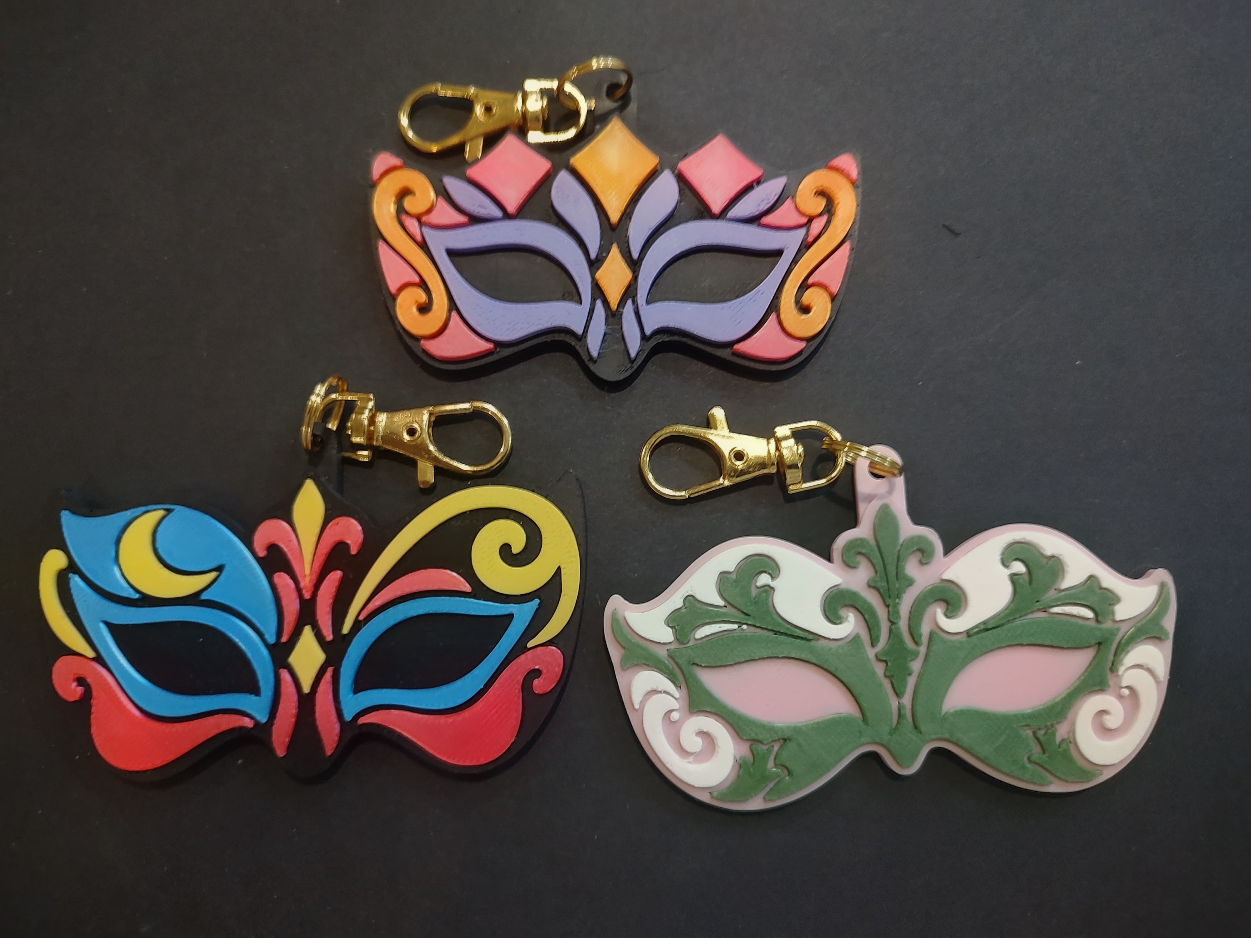 Three colorful MerchWT masquerade mask bag charms